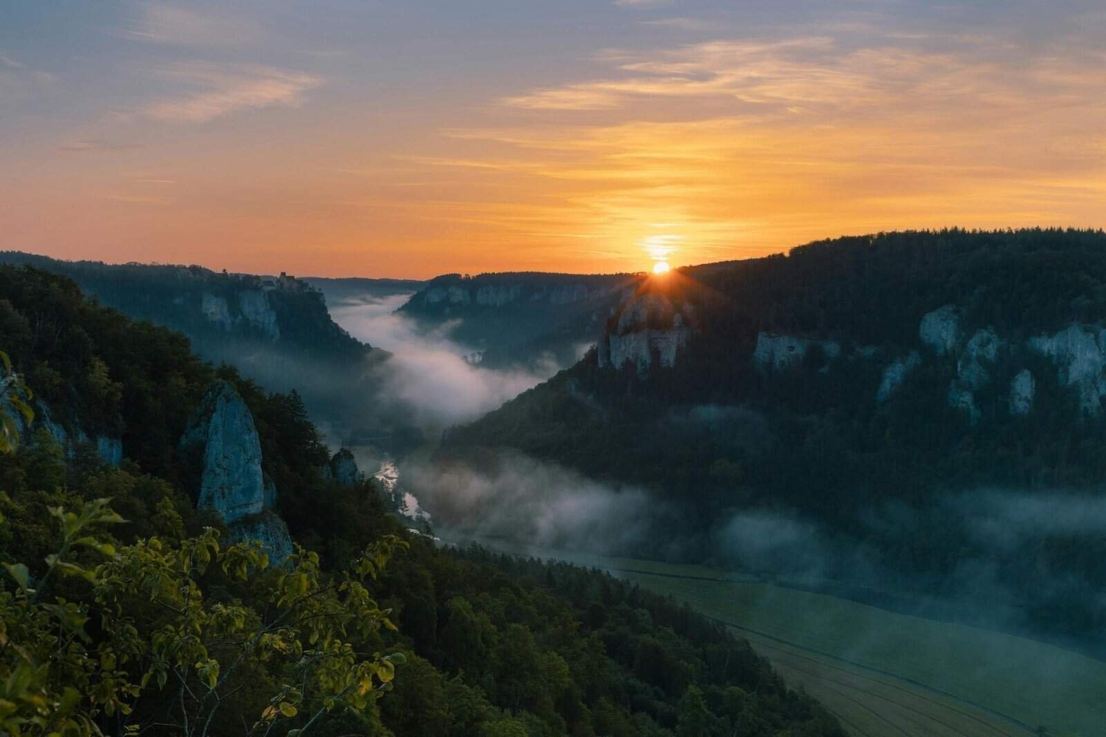 Sunrise over a lush green canyon with misty valleys and rocky cliffs, creating a serene and breathtaking landscape.